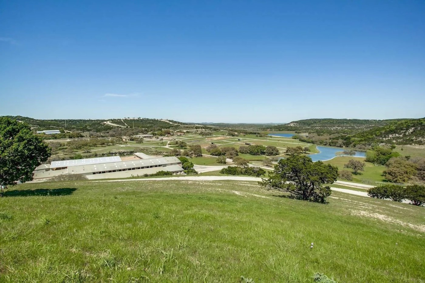 Elevated view across Double Diamond Ranch &mdash; pasture, lakes, and the arena complex in the Texas Hill Country